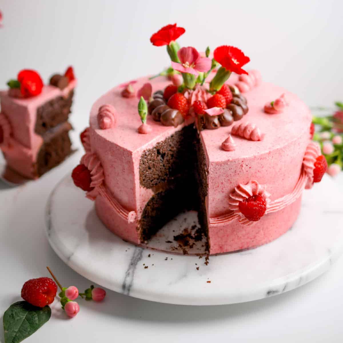 raspberry chocolate layer cake, round two layer pink cake with slice removed to reveal chocolate interior, flowers and raspberries on outside